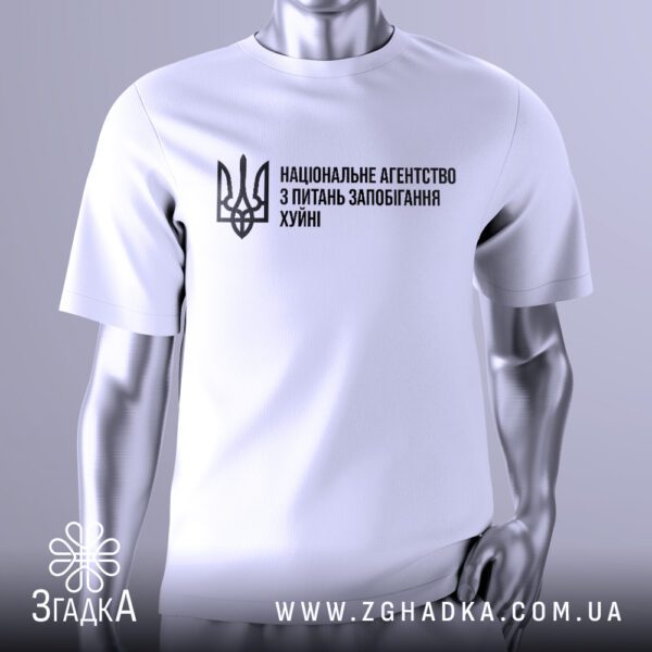 Біла футболка Агентство Запобігання Подарунок на сріблястому манекені, що демонструє принт з написом "НАЦІОНАЛЬНЕ АГЕНТСТВО З ПИТАНЬ ЗАПОБІГАННЯ ХУЙНІ" та українським гербом.