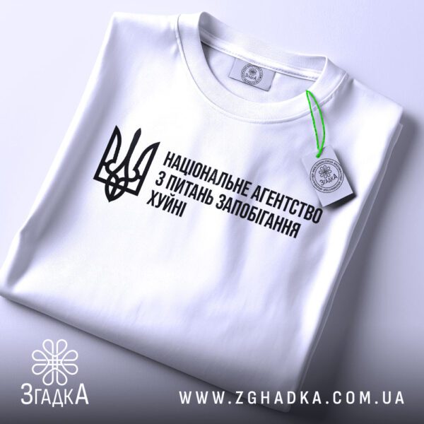 Складена біла футболка Агентство Запобігання Подарунок з гумористичним принтом та етикеткою "ЗГАДКА".