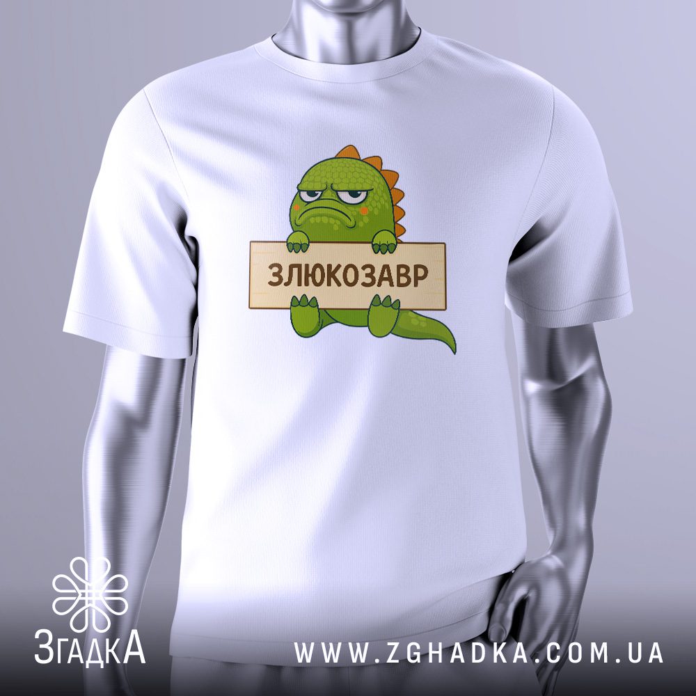 Біла футболка Злюкозавр Дракон Подарунок на сріблястому манекені, що демонструє принт милого зеленого динозаврика/дракона з сердитим обличчям та написом "Злюкозавр".