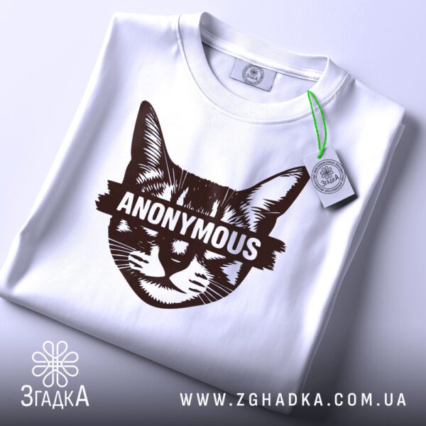 Складена біла футболка з принтом "анонімний стиль кота" та етикеткою "Згадка".
