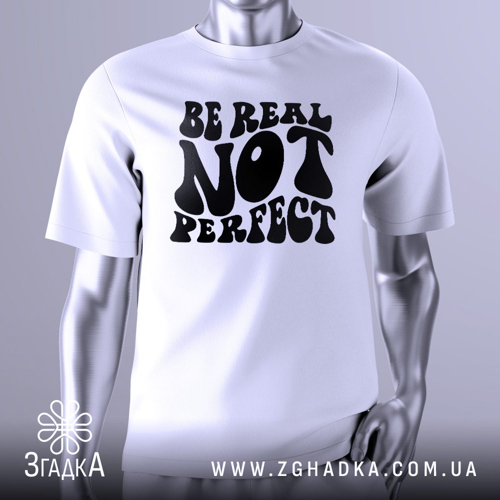 Біла футболка з чорним текстовим принтом у центрі. Напис "Be real not perfect" виконаний у стилізованому ретро-шрифті, де слова "real" і "perfect" виділені жирнішим накресленням. Футболка на сірому манекені.