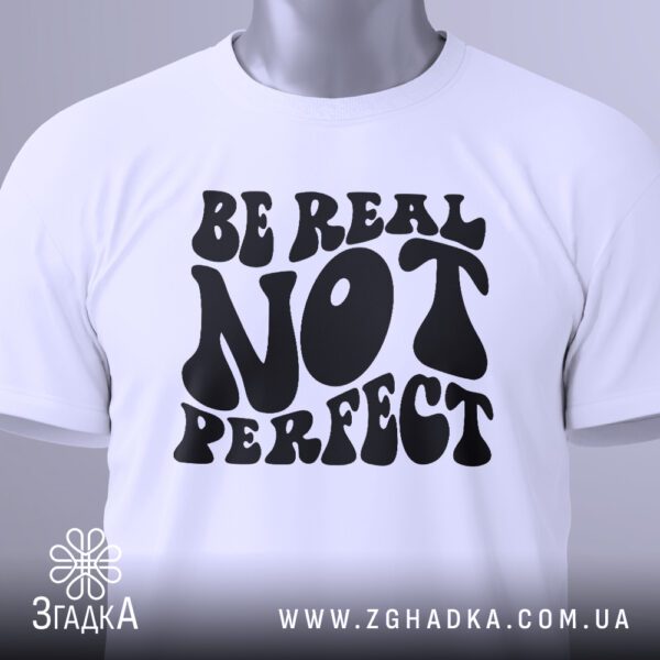 Крупний план принта "Be real not perfect" на білій футболці, що детально показує шрифти та їх стилізацію.
