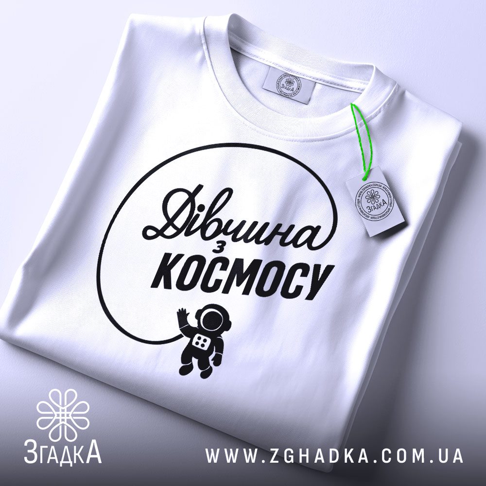 Складена біла футболка з принтом "дівчина з космосу" та етикеткою "Згадка".