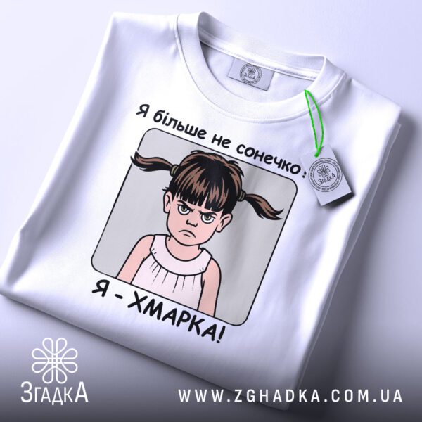 Складена біла футболка з принтом "дівчинка я хмарка" та етикеткою "Згадка".