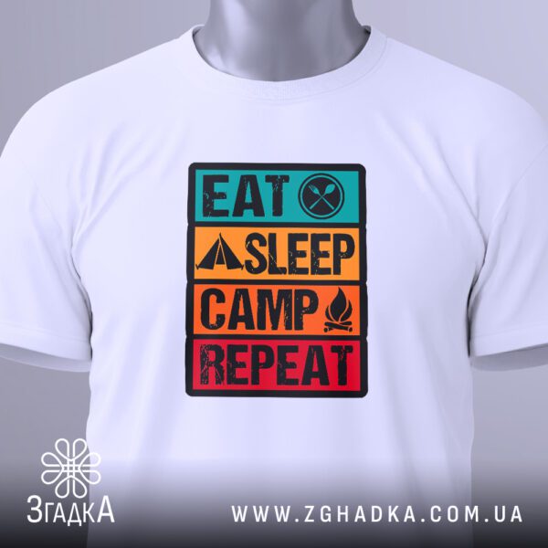 Крупний план кольорового принта "Eat Sleep Camp Repeat" на білій футболці, що детально показує слова та кольорові блоки.