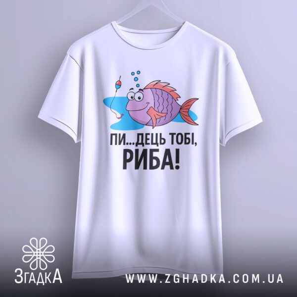 Біла футболка з кольоровим принтом веселої риби-рибалки та написом "ПИ...ДЕЦЬ ТОБІ, РИБА!", що висить на вішаку.