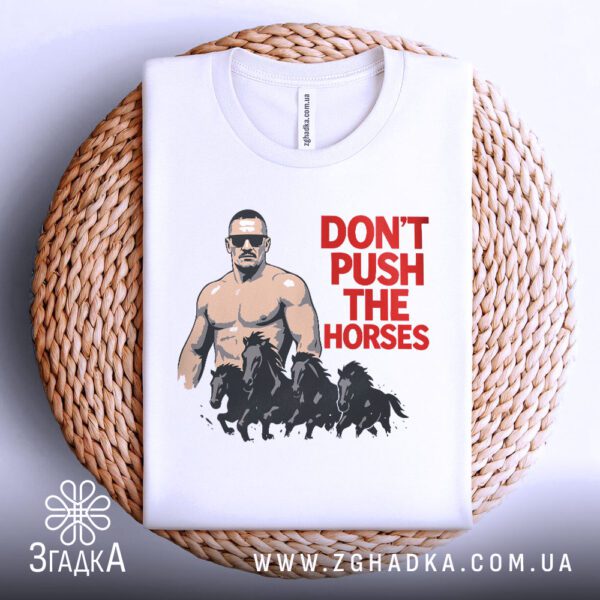 Біла футболка з принтом "don't push horses", акуратно складена на круглій дерев'яній поверхні.