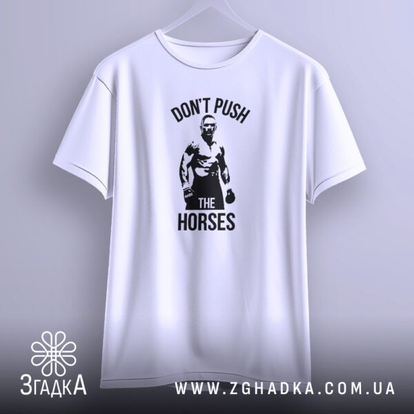 Біла футболка з принтом "don't push horses", що висить на білих плічках, демонструючи дизайн.