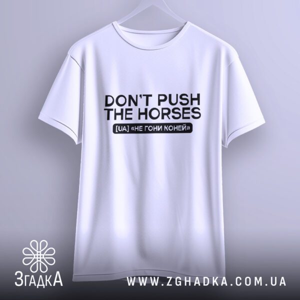 Біла футболка з принтом "Dont push the horses", що висить на білих плічках, демонструючи дизайн.