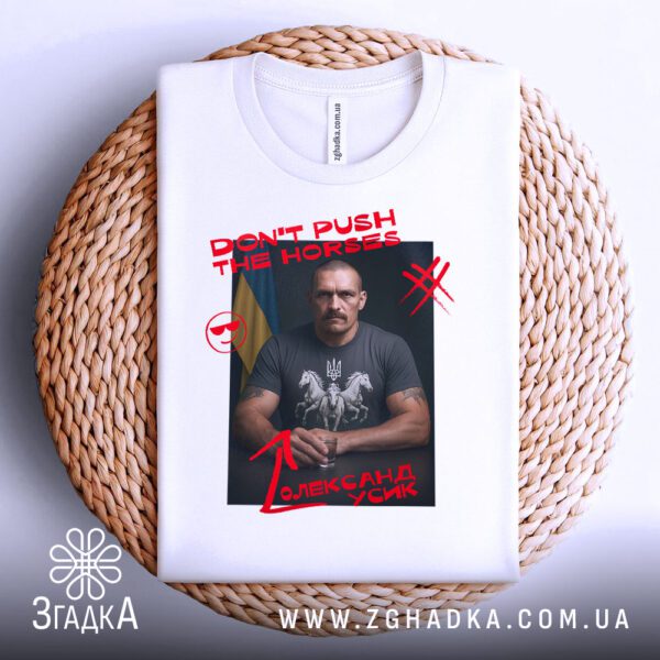 Біла футболка з принтом "don't push Усик", акуратно складена на круглій дерев'яній поверхні.