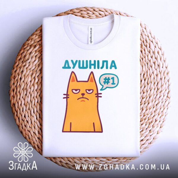 Біла футболка з принтом "душніла номер один", акуратно складена на круглій дерев'яній поверхні.