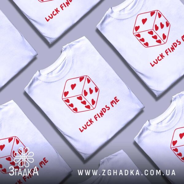 Кілька білих футболок з принтом "фарт завжди зі мною", складені стопкою або розкладені поруч на світлому фоні.