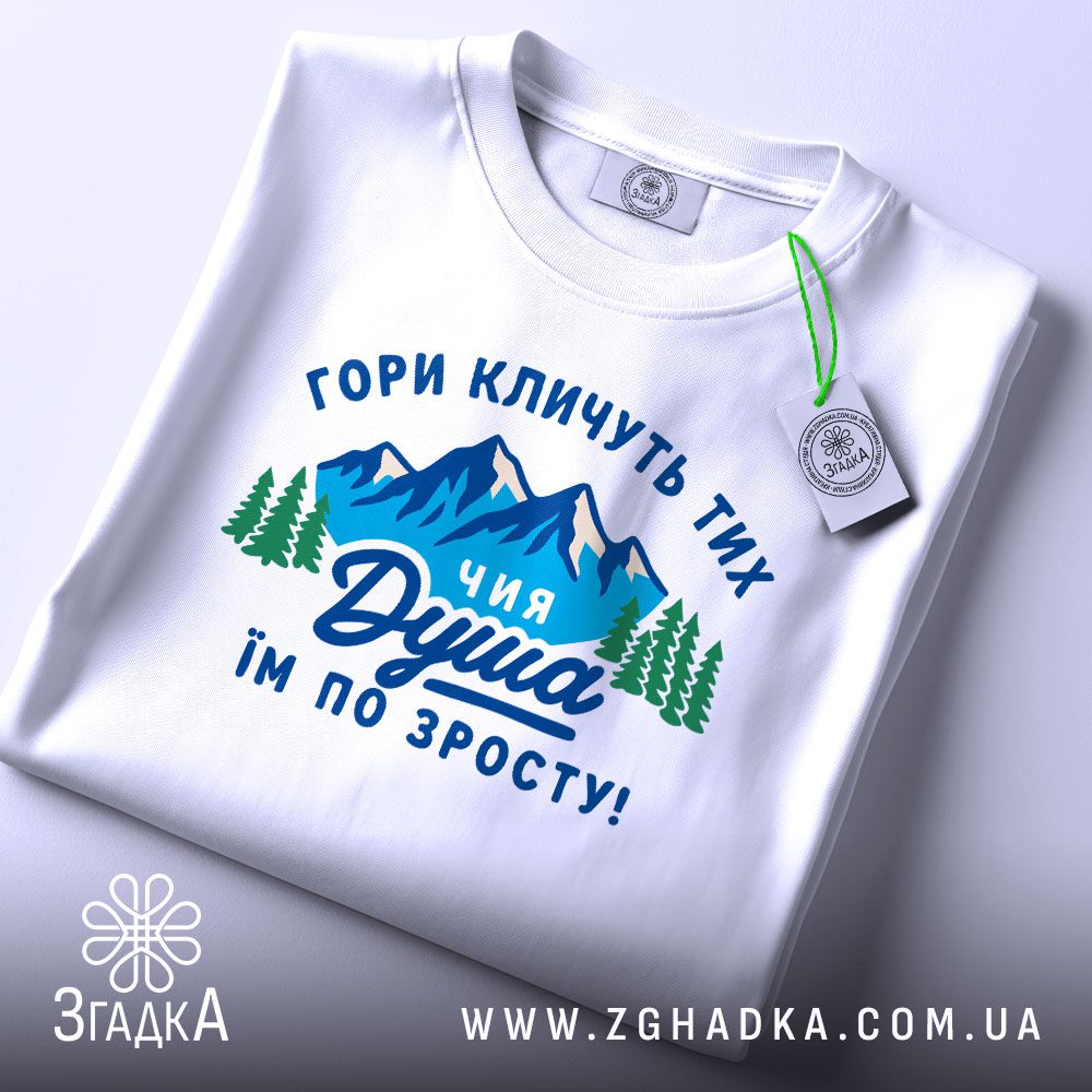 Складена біла футболка з принтом "гармонія з горами" та етикеткою "Згадка".