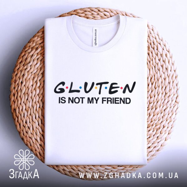 Біла футболка з принтом "Gluten is not my friend", акуратно складена на круглому плетеному підносі.