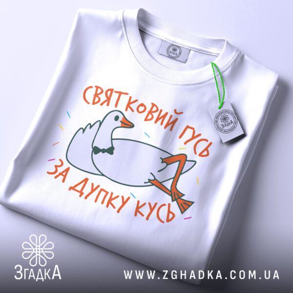 Складена біла футболка з принтом "гусь дупку кусь" та етикеткою "Згадка".