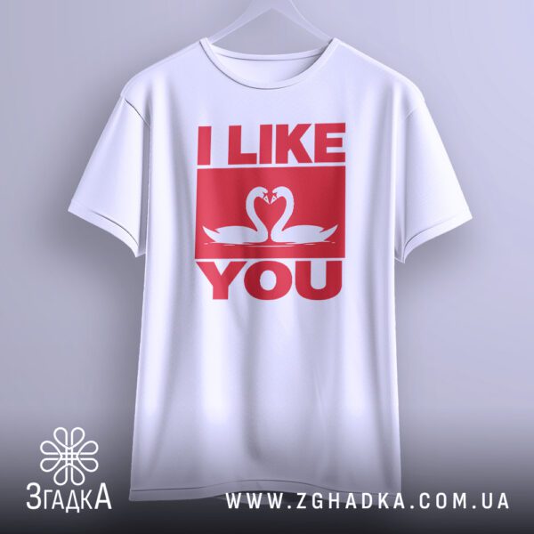Біла футболка з принтом "I LIKE YOU", що висить на білих плічках, демонструючи дизайн.