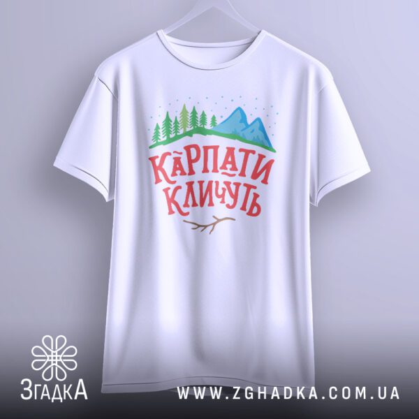 Біла футболка з принтом "КАРПАТИ КЛИЧУТЬ", що висить на білих плічках.