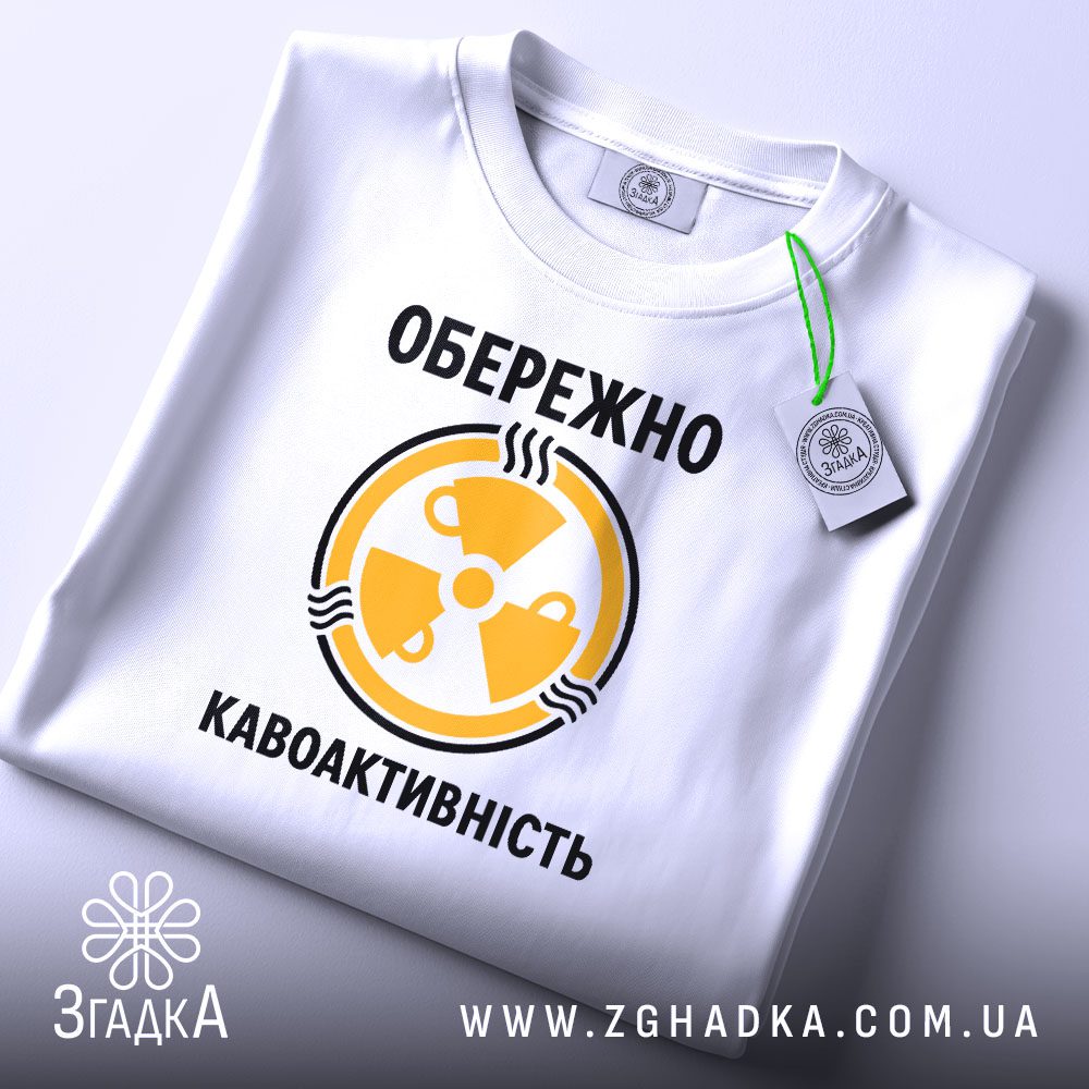 Складена біла футболка з принтом "кавоактивність з іронією" та етикеткою "Згадка".