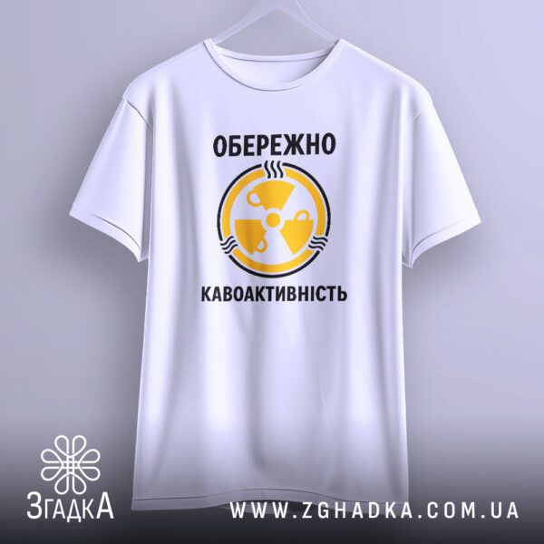 Біла футболка з принтом "кавоактивність з іронією", що висить на білих плічках, демонструючи дизайн.