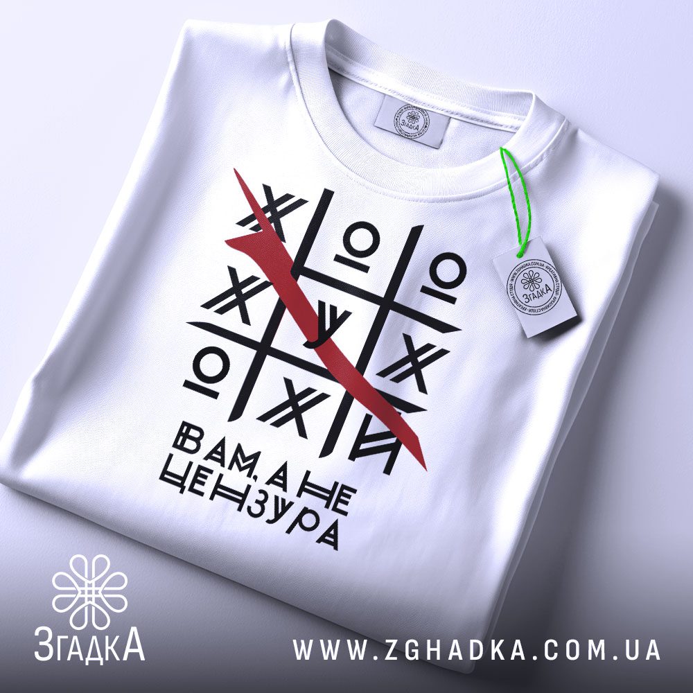 Складена біла футболка з принтом "хрестики нулики жарт" та етикеткою "Згадка".