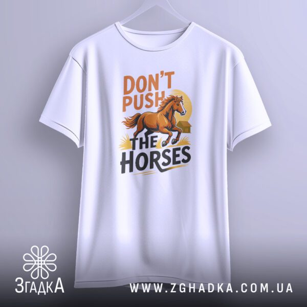 Біла футболка з принтом "кінь Don’t push", що висить на білих плічках, демонструючи дизайн.