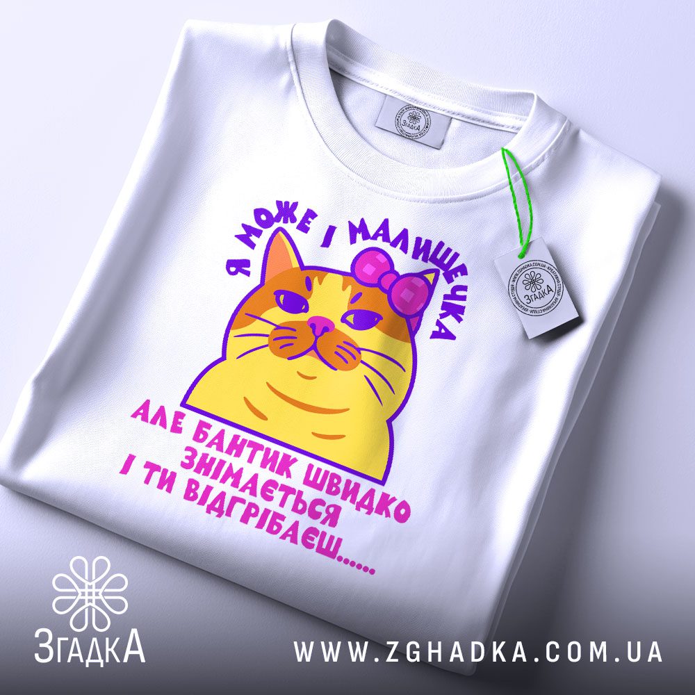 Складена біла футболка з принтом "кішка з характером" та етикеткою "Згадка".