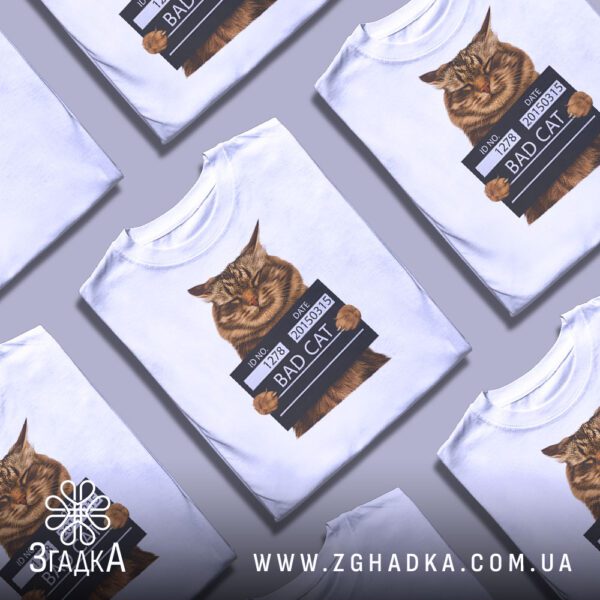 Кілька білих футболок з принтом "кіт bad cat", складені стопкою або розкладені поруч на світлому фоні.