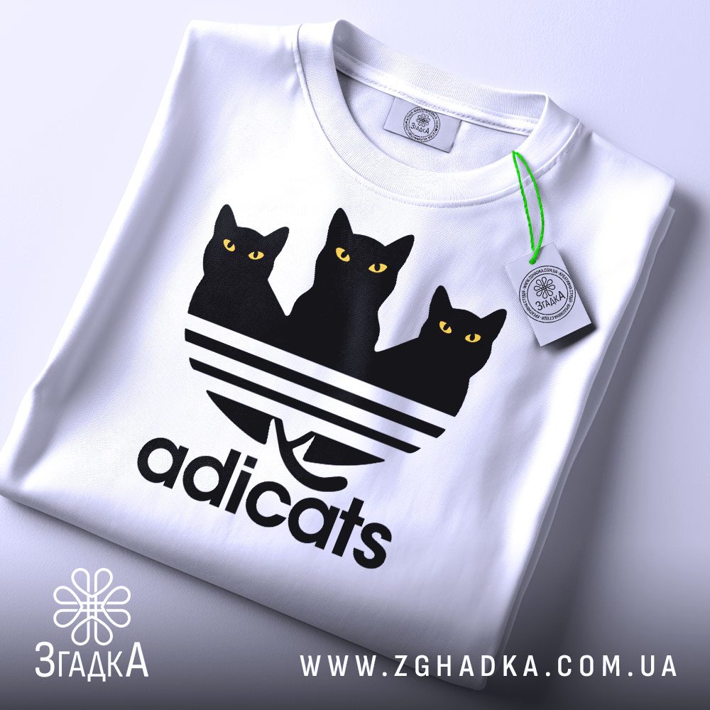 Складена біла футболка з принтом "кіт пародія Adidas" та етикеткою "Згадка".