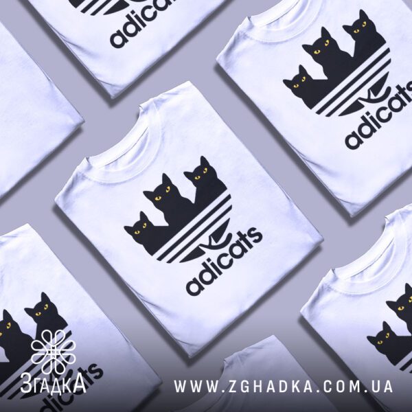 Кілька білих футболок з принтом "кіт пародія Adidas", складені стопкою або розкладені поруч на світлому фоні.