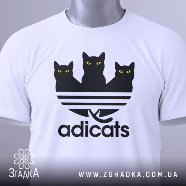 Крупний план принта "кіт пародія Adidas" на білій футболці, що детально показує текст "adicats" та стилізовані фігури котів.