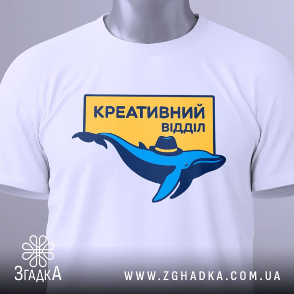 Крупний план принта "креативний відділ стиль" на білій футболці, що детально показує кита та напис.