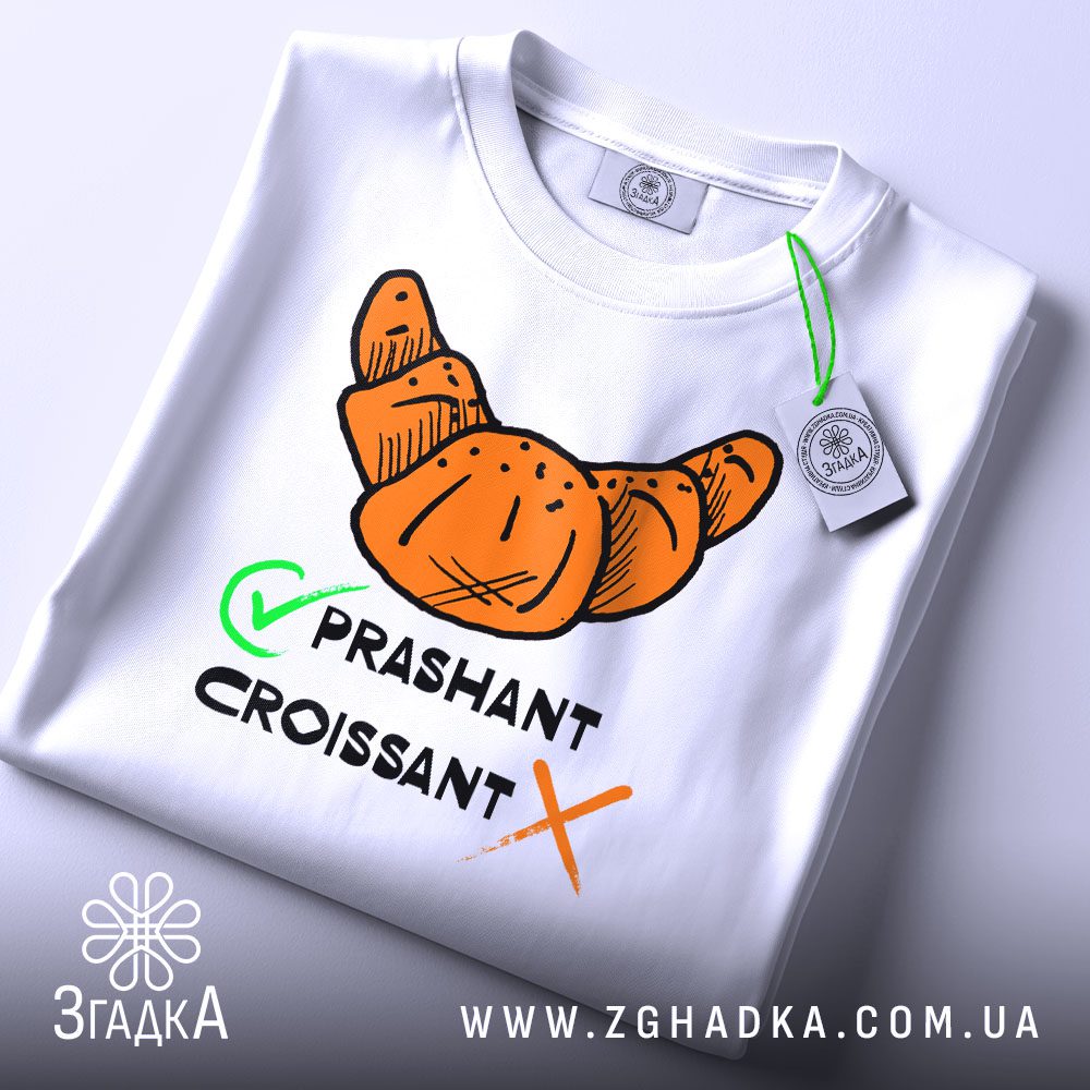 Складена біла футболка з принтом "круасан став прашант" та етикеткою "Згадка".