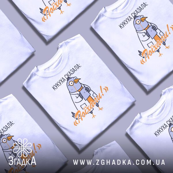 Кілька білих футболок з принтом "Кукуха сказала поїхали", складені одна на одну або розкладені поруч на сірому фоні.