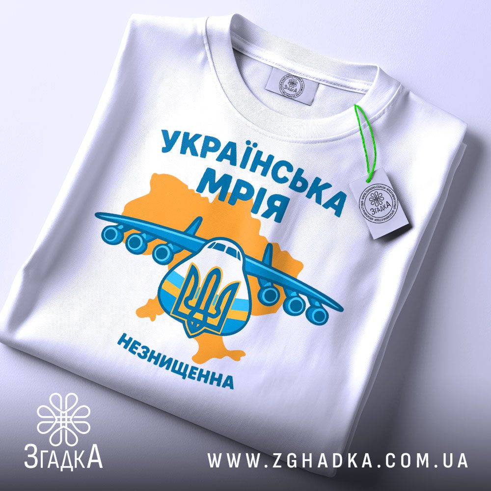 Складена біла футболка з кольоровим графічним принтом "Українська Мрія Незнищенна" та етикеткою "Згадка".