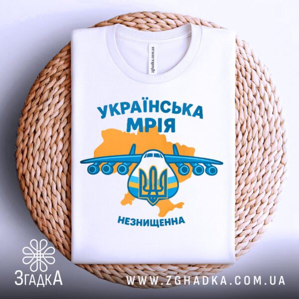 Біла футболка з принтом "Українська Мрія Незнищенна", акуратно складена на круглому плетеному підносі.