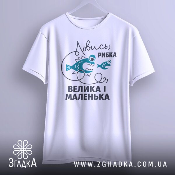Біла футболка з принтом "Ловись рибка велика-велика", що висить на вішаку.