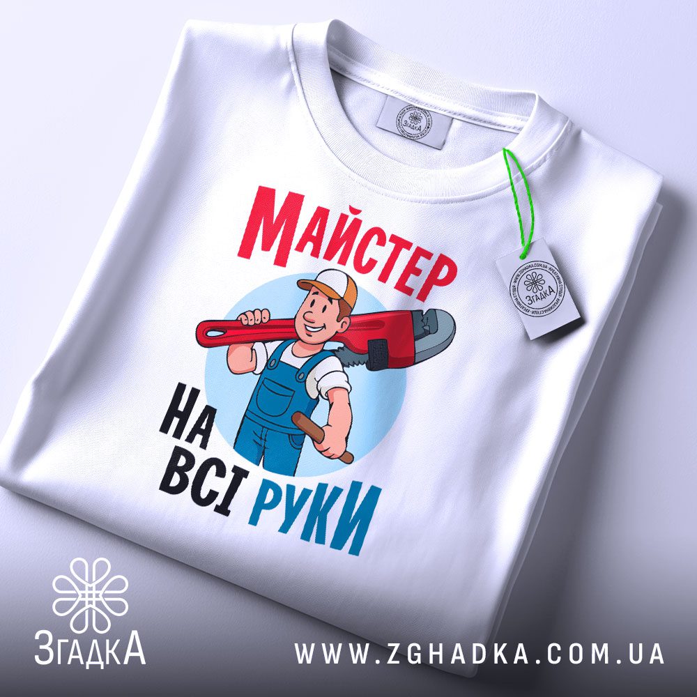 Складена біла футболка з чорним текстовим принтом "Майстер на всі руки" та етикеткою "Згадка".