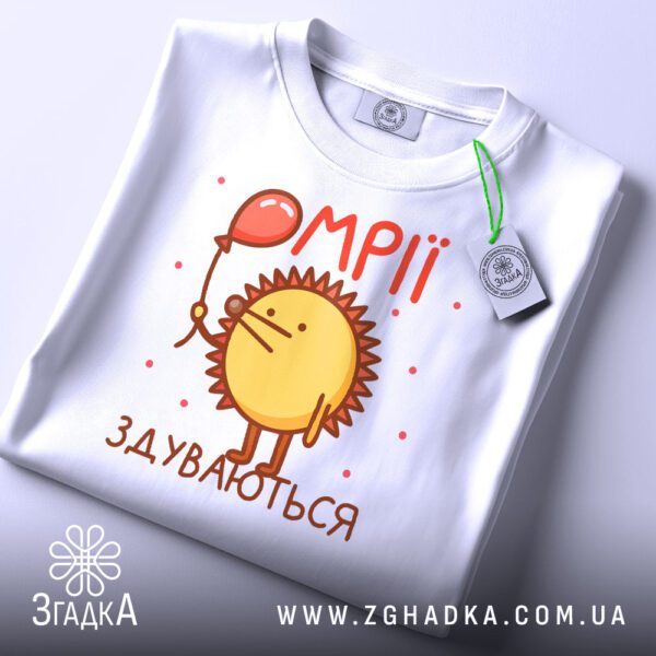 Складена біла футболка з принтом "мрії здуваються їжак" та етикеткою "Згадка".