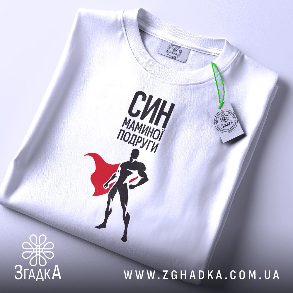 Складена біла футболка з принтом "СИН МАМИНОЇ ПОДРУГИ" та фірмовою етикеткою "Згадка".