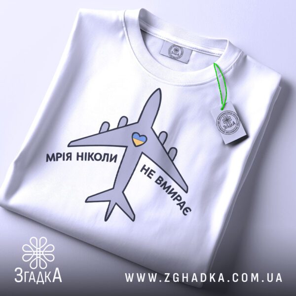 Складена біла футболка з принтом "мрія не вмирає" та етикеткою "Згадка".