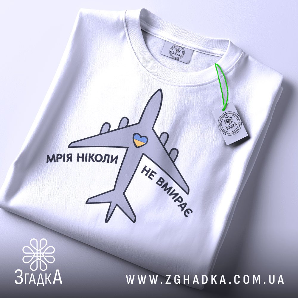 Складена біла футболка з принтом "мрія не вмирає" та етикеткою "Згадка".