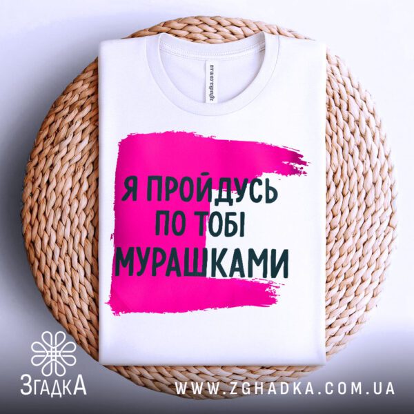 Біла футболка з принтом "мурашки по шкірі", акуратно складена на круглій дерев'яній поверхні.