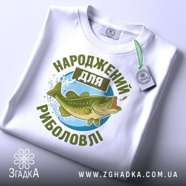 Складена біла футболка з принтом "Народжений для риболовлі" та етикеткою "Згадка".