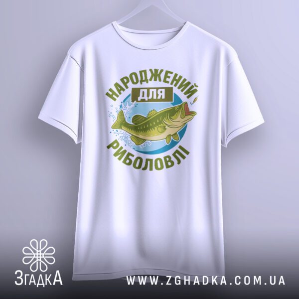Біла футболка з принтом "Народжений для риболовлі", що висить на вішаку.