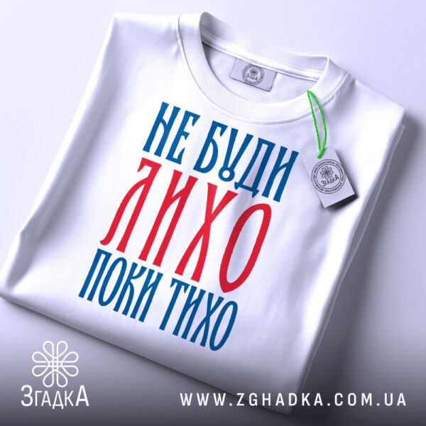 Складена біла футболка з принтом "не буди лихо" та етикеткою "Згадка".