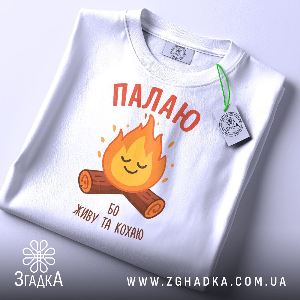 Складена чорна футболка з білим текстовим принтом "Палаю бо живу та кохаю" та етикеткою "Згадка".