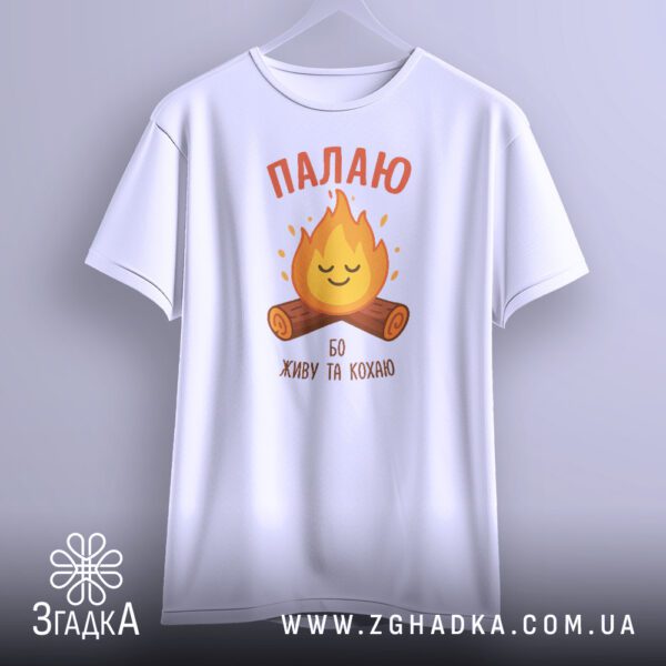 Чорна футболка з принтом "Палаю бо живу та кохаю", що висить на чорних плічках.