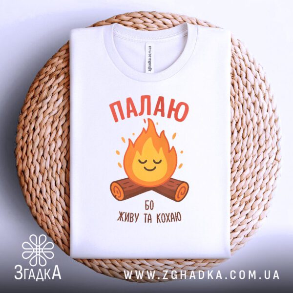 Чорна футболка з принтом "Палаю бо живу та кохаю", акуратно складена на темному плетеному підносі.