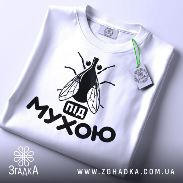 Складена біла футболка з принтом "під мухою жарт" та етикеткою "Згадка".
