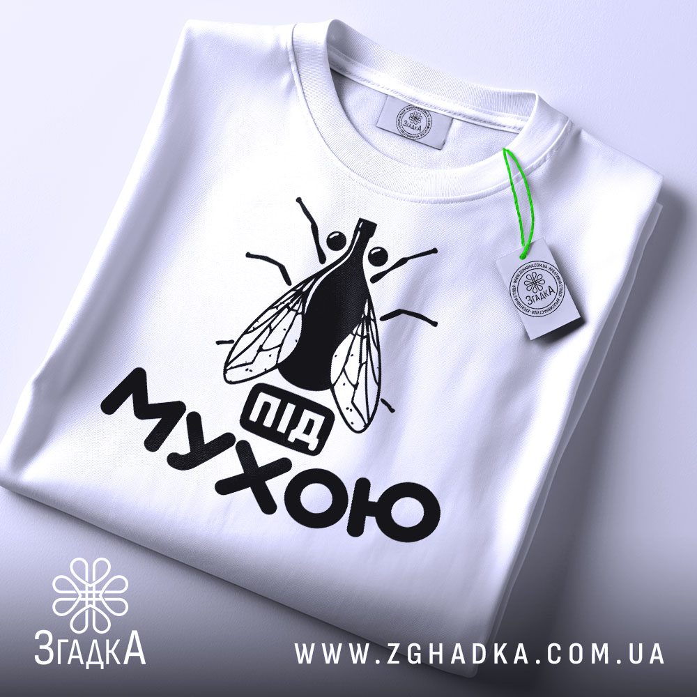 Складена біла футболка з принтом "під мухою жарт" та етикеткою "Згадка".